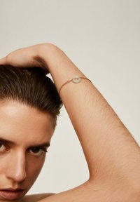 Pulsera de tono dorado con un centro de piedra circular y translúcida. El diseño es delicado con una fina cadena de metal y una textura suave.