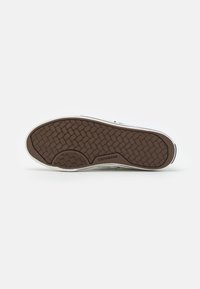 Brown rubber sneaker sole features a textured tread pattern with a white midsole and "Converse" branding on the side.