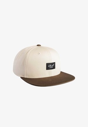 Beige baseball cap with brown flat brim and black rectangular logo patch on front reading "Reell est. 1997."