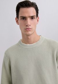 Pull en tricot vert clair avec un motif texturé, présentant un col rond côtelé et une coupe décontractée. Tissu lisse, détails de design minimaux.