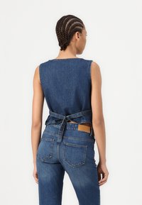 Denim top with a round neckline, sleeveless design, and tied back. Worn with matching high-waisted jeans featuring back pockets.