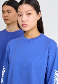 Königsblaue Langarm-T-Shirts aus Baumwolle mit Rundhalsausschnitt, ausgestattet mit weißen Textelementen auf den Ärmeln.