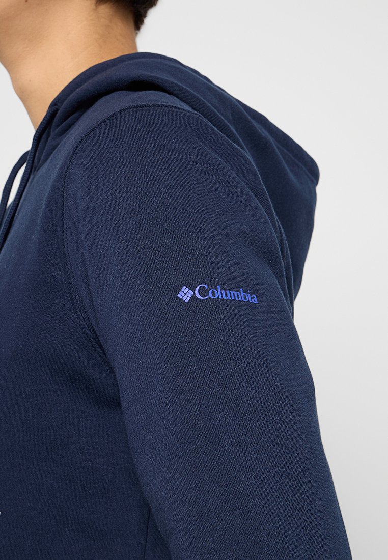 Felpa con cappuccio blu navy realizzata in tessuto morbido. Presenta un logo Columbia visibile in un contrastante azzurro chiaro sul lato sinistro della manica.