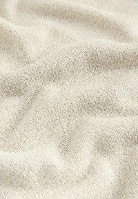 Gros plan sur un tissu beige tricoté avec des points texturés visibles et des plis doux formant de légères ondulations.