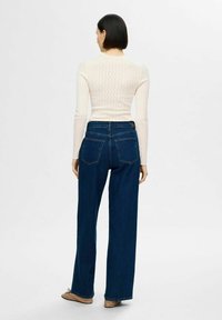 Ljust krämfärgat, stickat tröja med zick-zack-mönster, parat med högmidjade, blå vida byxor. Outfiten har en enkel design och en figurnära silhuett.