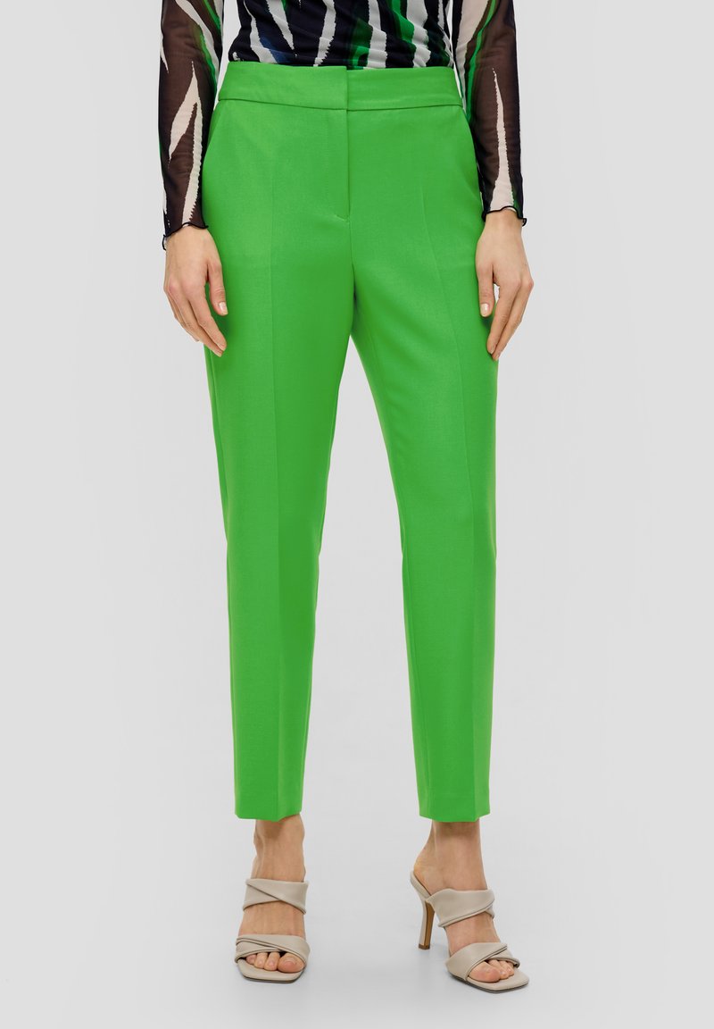 Svěží zelené kalhoty na míru s hladkou texturou, s plochým předním dílem, bočními kapsami a úzkým střihem. Kombinováno s tělovými sandály na podpatku.