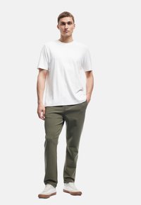 Hvid bomulds t-shirt, kortærmet; olivengrøn tapered bukser; hvide sneakers med tan såler; glat tekstur, afslappet design.