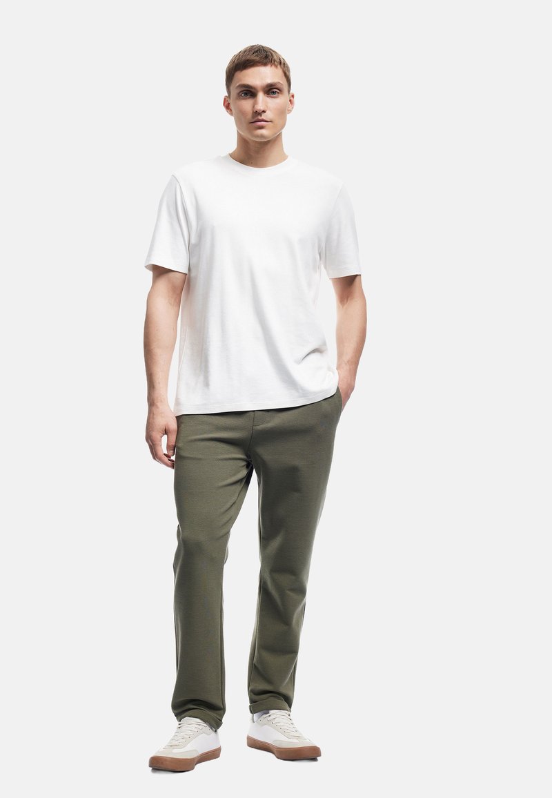 Hvid bomulds t-shirt, kortærmet; olivengrøn tapered bukser; hvide sneakers med tan såler; glat tekstur, afslappet design.
