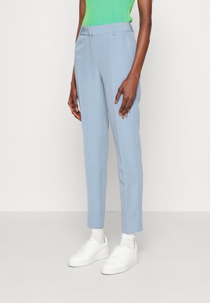 Pantalon ajusté bleu clair avec une texture lisse, plis à l'avant, poches latérales et un design cintré, associé à des baskets blanches.