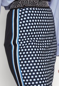 Leggings de sport noirs avec un motif à pois bleu et blanc, dotés d'une ceinture noire avec le texte "SPORTS" et de bandes latérales contrastantes.
