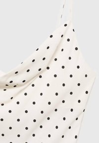 Haut blanc sans manches avec fines bretelles et pois noirs uniformément répartis sur le tissu.