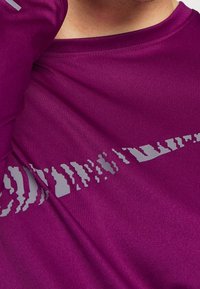 Lila Sport-langarmshirt mit einem kontrastierenden grauen abstrakten Muster über der Brust und einer glatten, leichten Stofftextur.