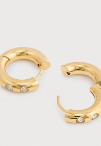 Ζευγάρι χρυσών σκουλαρικιών κρίκων με δύο μικρούς στρογγυλούς διαφανείς πολύτιμους λίθους τοποθετημένους σε κάθε σκουλαρίκι, εκτεθειμένα σε λευκό φόντο.