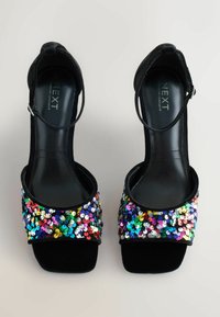 I sandali neri con tacco alto presentano una fascia per le dita decorata con paillettes multicolori. Il materiale appare liscio e riflettente, con una fascia per la caviglia.