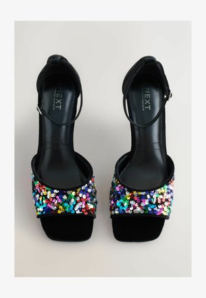 Fekete magassarkú szandálok csillogó, többszínű flitterekkel díszített lábujjrészes pánttal rendelkeznek. Az anyaga simának és fényesnek tűnik, és van rajta bokapánt.