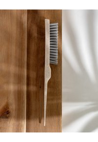 Spazzola con manico beige chiaro e setole grigie, con un'estremità affusolata. Posizionata su una superficie in legno testurizzata.