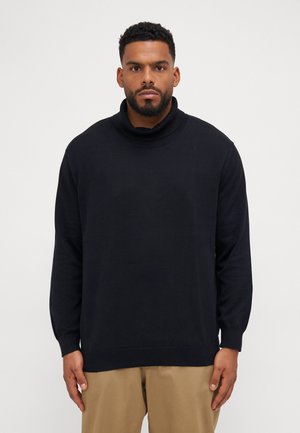 Pull à col roulé noir en tricot avec des manches longues, un col côtelé et une coupe décontractée. Assorti avec un pantalon beige.