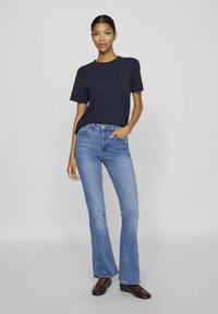 Navy kortermet t-skjorte kombinert med lyseblå utsvingte jeans og brune snørebåndssko, med en avslappet passform og subtile detaljer.
