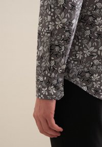 Koszula z długim rękawem o szarym wzorze kwiatowym, z czarno-białymi kwiatami. Zapięcie na guziki przy mankiecie oraz lekko zwężany krój. Gładka struktura materiału.