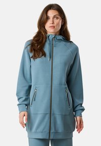 Lichtblauwe zip-up hoodie met een hoge kraag, twee voorzakken met rits en gouden accenten. Gemaakt van zacht materiaal met een gladde textuur.