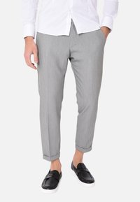 Pantaloni grigi realizzati in un materiale leggero, con un taglio slim e orli arrotolati, abbinati a scarpe nere senza lacci.