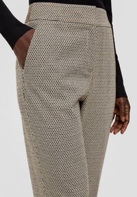 Pantalons texturés taille haute en beige et noir, avec un motif géométrique, des poches latérales et une coupe ajustée.