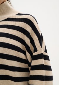 Pulover rayat cu guler înalt, având dungi orizontale late de crem și negru. Textură ribbed și o croială lejeră.
