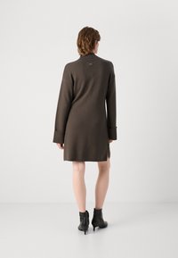 Καφέ πλεκτό φόρεμα με ψηλό λαιμό, ριγωτούς μανίκους και πλαϊνές σχισμές. Συνδυασμένο με μαύρες μποτίνια μέχρι τον αστράγαλο, με λεπτές μύτες και τακούνια.