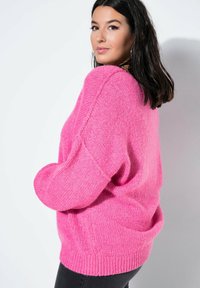 Różowy, oversize sweter wykonany z miękkiej, teksturowanej dzianiny, z prążkowanymi mankietami i dołem, charakteryzujący się luźnym krojem i opadającymi ramionami.
