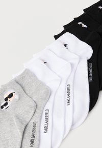 Trys poros kojinių pilkos, baltos ir juodos spalvos. Kiekvienoje kojinėje pavaizduotas personažas su akiniais nuo saulės, šalia išsiuvinėtas prekės ženklas.