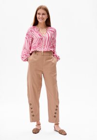 Roze en crèmekleurige blouse met een print en een neklint, gecombineerd met beige broek met zijknopen en een relaxte pasvorm. Geassocieerd met sandalen met bandjes.