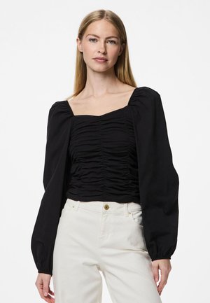 Svart bluse med firkantet utringning, rynket front og lange puffede ermer; brukt med off-white bukser, med knappdetalj i livet.