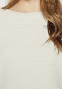 Light cream textured top with a ribbed pattern and a wide neckline. Features soft fabric with subtle detailing, suitable for casual wear.