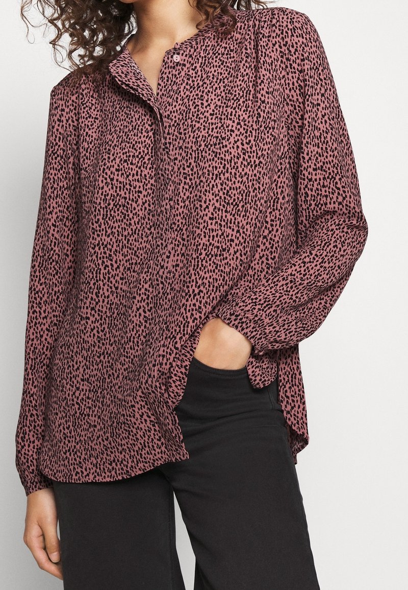 Blouse rose à manches longues avec imprimé léopard noir, design sans col, poche avant visible, poignets froncés et ourlet incurvé.