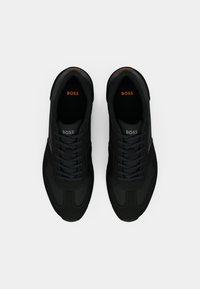 Par de ténis pretos BOSS com atacadores, vistos de cima sobre um fundo branco, mostrando os logótipos da BOSS no interior e na língua.