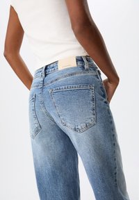 Jeans en denim bleu clair avec une coupe décontractée, dotés de poches arrière, d'une taille simple et d'une texture légèrement décolorée.