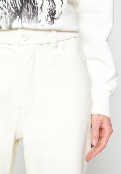 Λευκά, καλοραμμένα παντελόνια με λεία υφή, που διαθέτουν κλείσιμο με κουμπί και πλαϊνές τσέπες, συνδυασμένα με ένα ανοιχτόχρωμο, γραφικό φούτερ.