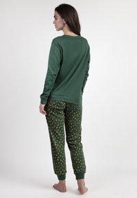 Top verde de manga larga con escote redondo combinado con pantalones de pijama verdes que presentan un estampado floral amarillo. Materiales suaves y casuales.