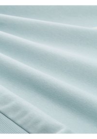 Tissu doux bleu clair avec des plis légers et un ourlet côtelé, suggérant un vêtement tricoté ou un tissu de sweat-shirt.