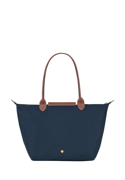Navy nylon tote bag with brown leather handles and accents, featuring a zip top closure and a gold logo detail at the bottom.