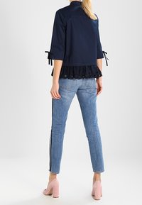 Mörkblå jacka med trekvartslånga ärmar och volangkant, kombinerad med ljusblå jeans med sidostrip och rosa högklackade skor.