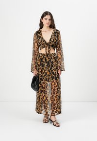 Prozirni top s uzorkom leopard tiska i vezanjem sprijeda, uparen s odgovarajućom suknjom. Crna torba i sandale s vezicama upotpunjuju izgled. Dominantne boje su smeđa i crna.