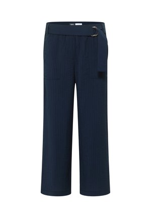 Personne portant un pantalon bleu marine texturé avec une grande poche plaquée et une ceinture assortie en tissu avec boucle anneau en D argentée.