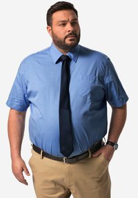 Ljusblå kortärmad skjorta med en ficka, matchad med en mörk slips. Beigefärgade byxor och ett svart bälte kompletterar outfiten.