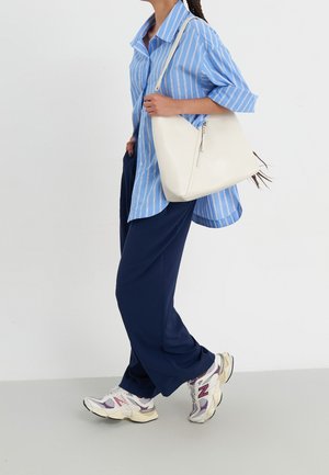Chemise oversize à rayures bleues et blanches, pantalon bleu marine et sac à épaule beige. Baskets blanches sportives avec des accents violets. Textures lisses.