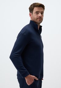 Granatowy sweter z zamkiem na ćwierć w miękkim materiale, z długimi rękawami, prążkowanymi mankietami i luźnym krojem. Czysty design bez widocznych wzorów czy logotypów.