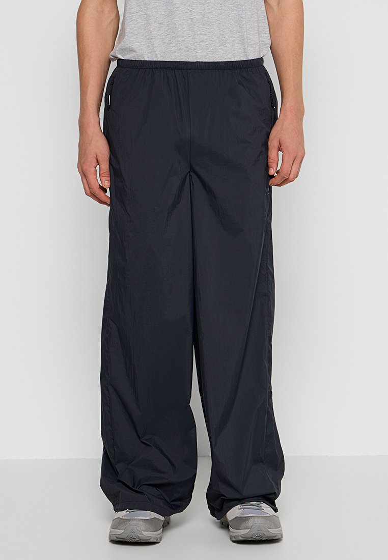 Zwarte, lichtgewicht, ongevoerde broek met een wijduitlopende pasvorm en elastische tailleband. Bevat zijzakken en een gladde, licht glanzende textuur.