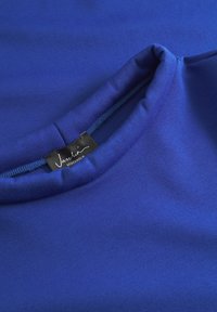 Blaue Baumwoll-T-Shirt mit rundem Ausschnitt. Der Stoff ist glatt und leicht dehnbar. Mit einem Etikett versehen, das "Vaslin Stockholm" zeigt.