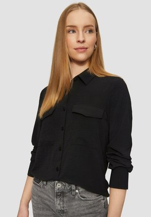 Zwarte button-up shirt met een gestructureerde afwerking, voorzien van twee borstzakken en lange mouwen die bij de manchetten zijn opgerold. Draagt het met grijze jeans.