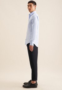 Camicia azzurro chiaro con colletto e maniche lunghe, abbinata a pantaloni neri a sigaretta e scarpe eleganti nere, mostrata in profilo laterale.